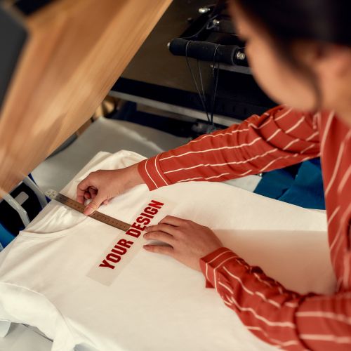 Get it customized. Cropped shot of woman trying on, moving advertisement sticker with text while preparing it to be printed on a T-Shirt